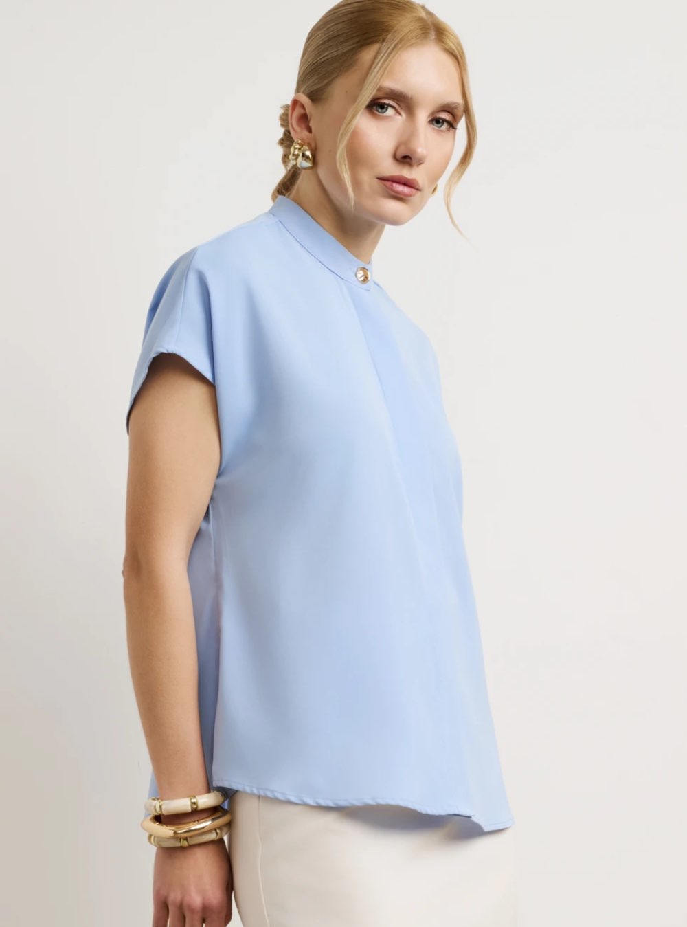 Γυναικείο πουκάμισο σχεδιασμένο με minimal αισθητική και ριχτή εφαρμογή. Διαθέτει μάο γιακά με διακριτικό διακοσμητικό κουμπί στο λαιμό. Κλείσιμο με κρυφά κουμπιά σε όλο το μήκος. Διαθέτει κοντό μανίκι. Το ύφασμα έχει απαλή υφή.